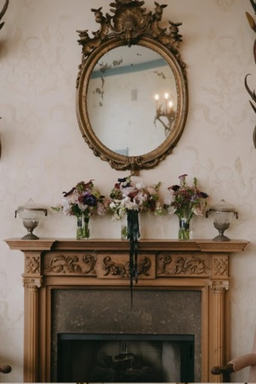 Bridal party bouquets displayed on a carved wood mantel beneath an oval gilded mirror