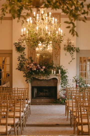 A wedding ceremony before a stone fireplace dressed in cascading florals beneath a crystal chandelier