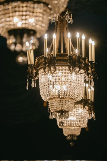 Antique crystal chandeliers glowing with candlelight at an elegant wedding reception