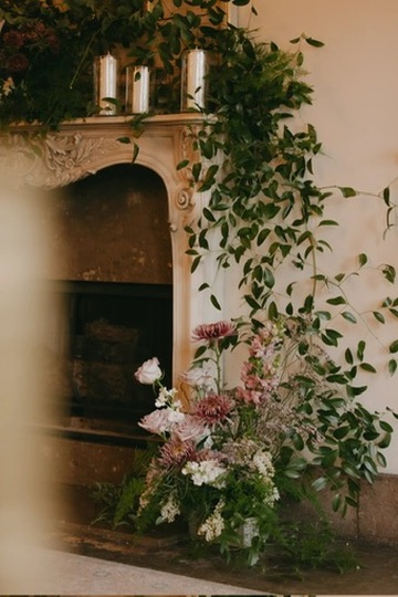 Romantic fireplace florals with pillar candles and cascading greenery designed in-house