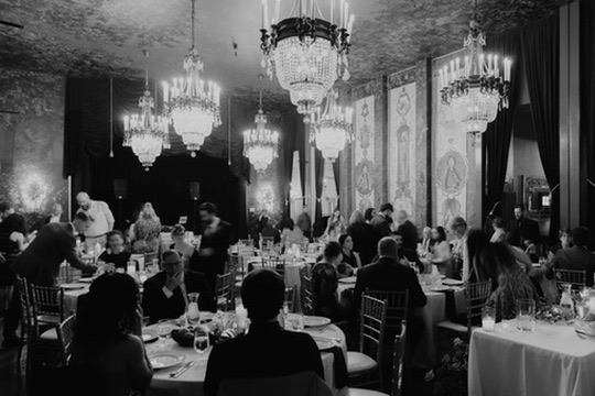 A grand ballroom glittering with crystal chandeliers during a black-tie wedding reception, in black and white
