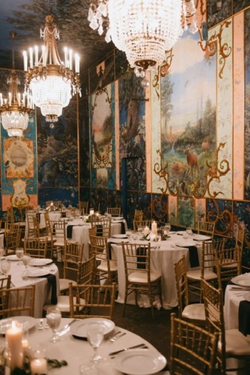 An opulent reception room with hand-painted murals, crystal chandeliers and gold chiavari chairs set for dinner