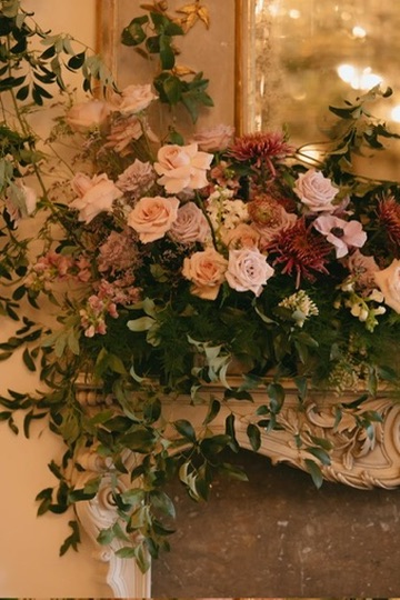 A close-up of blush garden roses, mauve dahlias and greenery on a carved marble mantel
